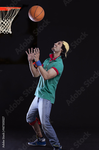 Full length of funky young man tossing basket ball against black background 