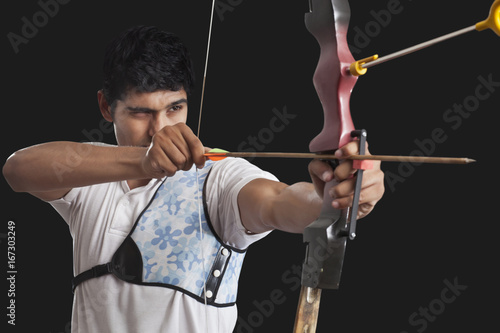 Young man aiming bow and arrow isolated over black background