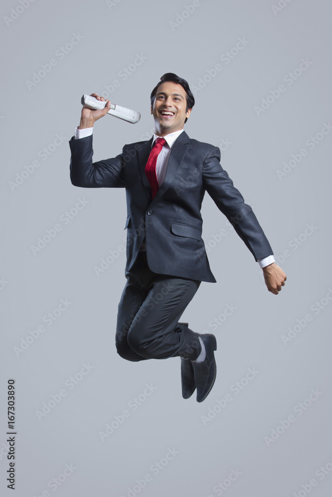 Full length of successful businessman with newspaper jumping over gray background Full length of successful businessman with newspaper jumping over gray background