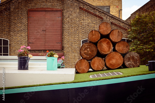 Stack of wood logs and watering cans with flowers on a narrow boat on a London canal