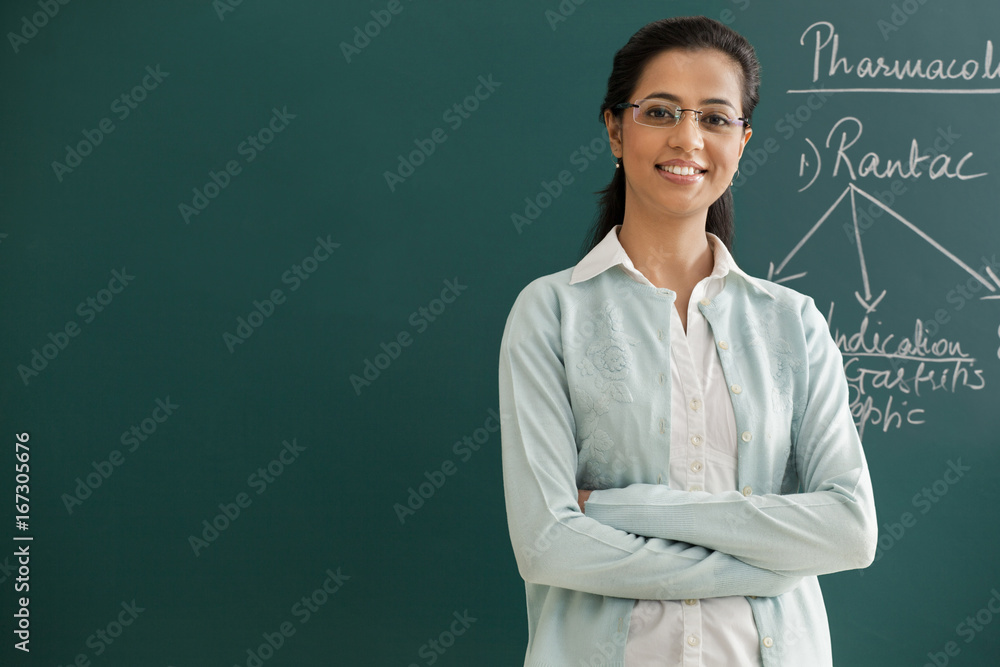 Portrait of an elementary school teacher with arms crossed standing against green board Portrait of an elementary school teacher with arms crossed standing against green board