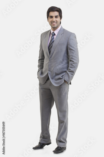 Full length portrait of young businessman with hands in pockets standing against white background 