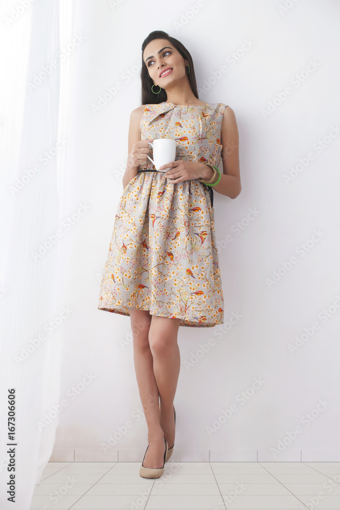 Thoughtful young woman with coffee cup leaning against white wall Thoughtful young woman with coffee cup leaning against white wall