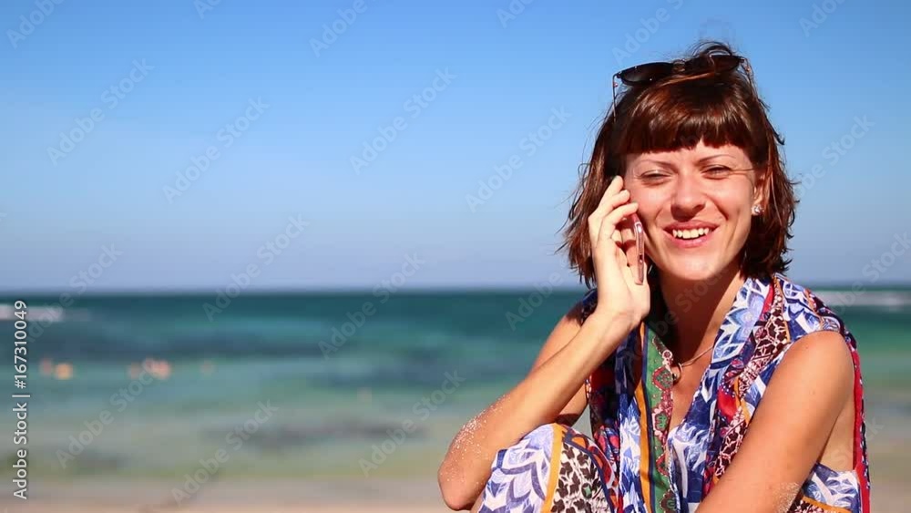 Woman using mobile cell smart phone laughing on beach. Girl in bikini using smartphone happy. Tropical Bali island, Indonesia.