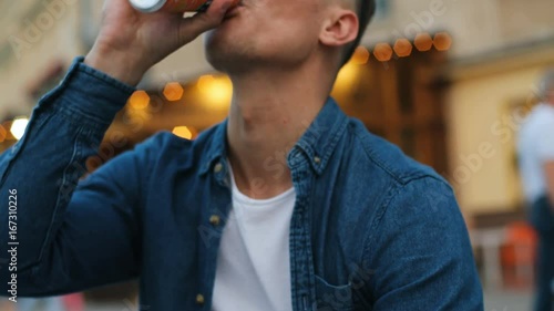 Portrait of attractive man drinking fanta from the bottle on the city background. Close up shot.