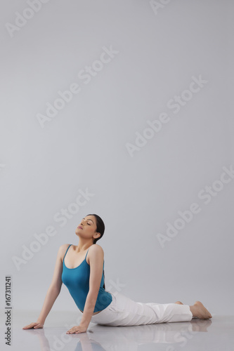 Young woman doing yogic 'sun salutation' isolated over gray background