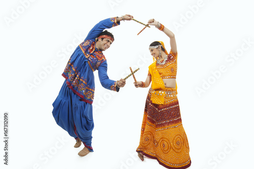 Young couple in traditional wear performing Dandiya Raas over white background
