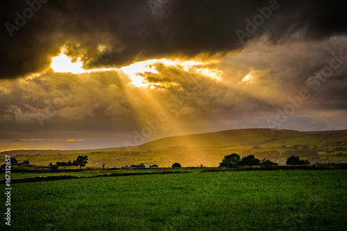 Summer sunset over landcape with sun rays through clouds