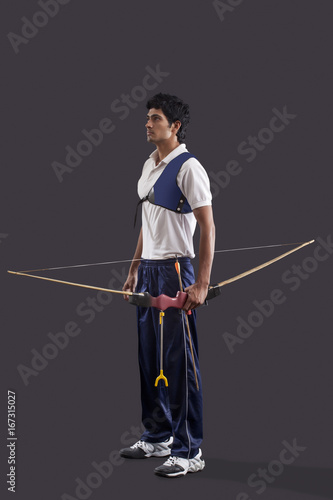 Full length of young male archer with bow and arrow over gray background