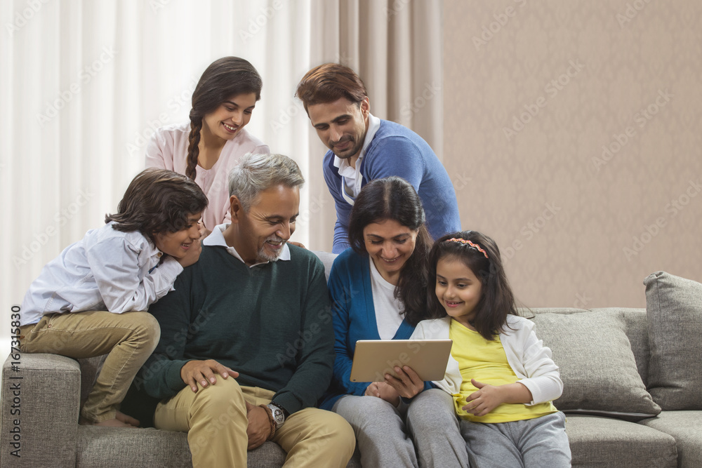 Happy Family looking at digital tablet while sitting on sofa Happy Family looking at digital tablet while sitting on sofa
