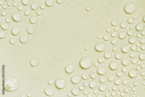 Big and small water drops on yellow background. Closeup.