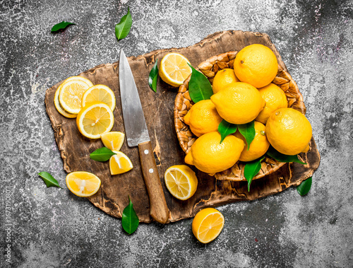 Fresh lemons in a basket with a knife on a cutting Board.