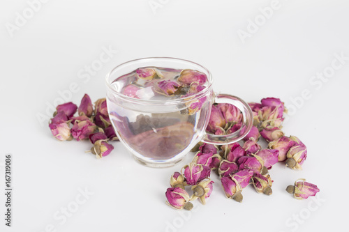 A cup of rose tea with dried rose flower on white background.