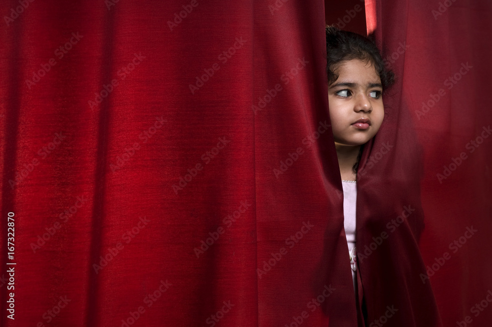 Little girl peeking out from a curtain 