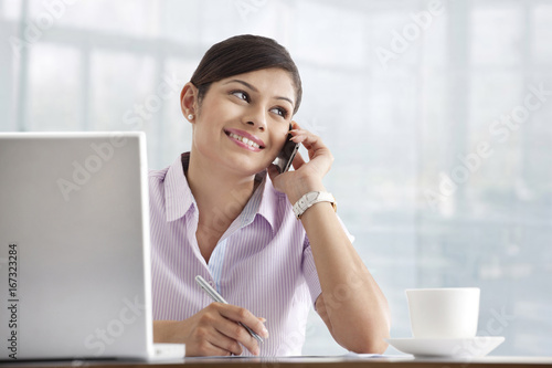 Happy young female executive using cell phone at her desk 