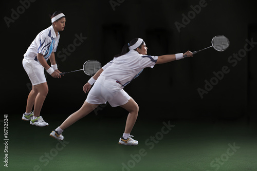 Profile shot of young women playing doubles badminton over black background