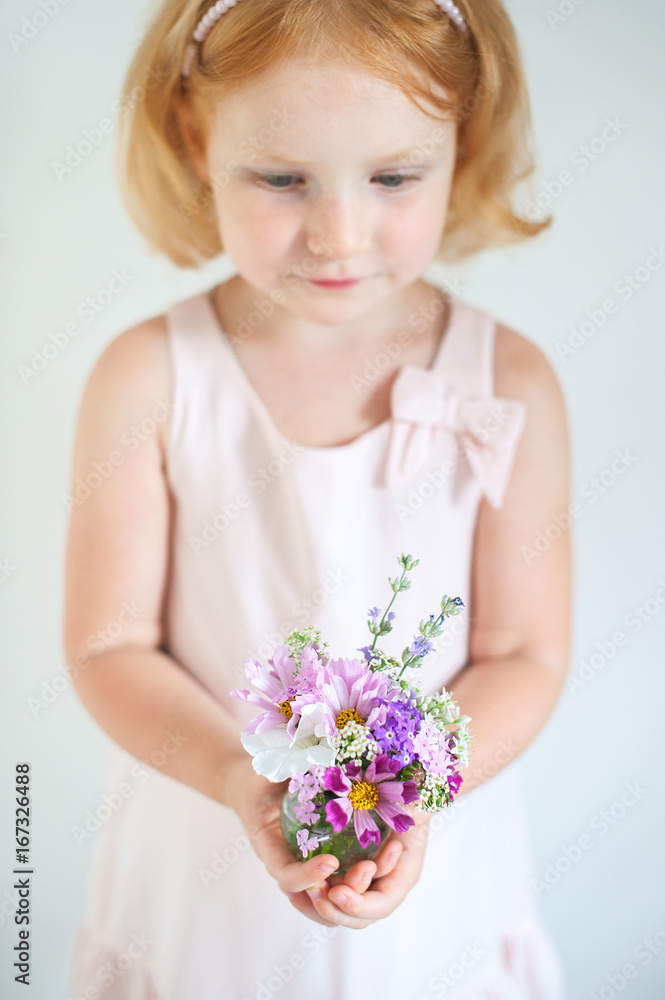 Beautiful red-haired child holding a bouquet of summer flowers Beautiful red-haired child holding a bouquet of summer flowers