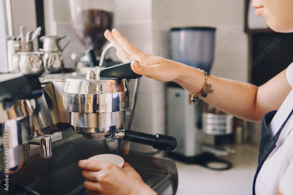 Closeup of young Caucasian barista hands holding paper cup making coffee using  coffee machine. Woman pouring coffee from professional espresso machine. Toned with film filters.