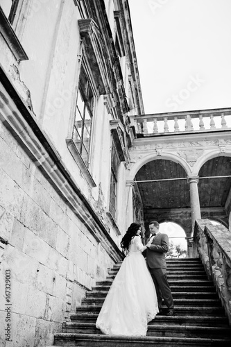 Awesome newly married couple enjoying each other s company on the stairs of old castle on a rainy wedding day. Black and white photo.