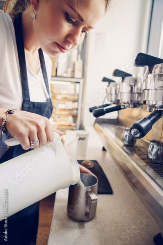 Closeup macro shot of Caucasian woman hands making coffee. Barista pouring hot milk in coffee metal jug.