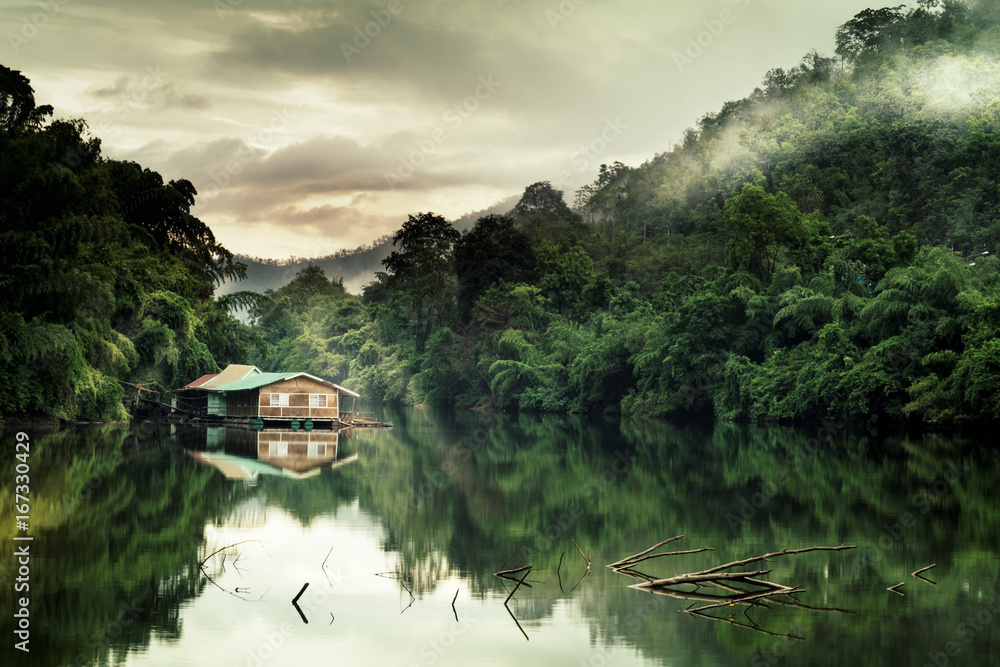 Fototapeta premium Mountain forest with fog and houseboat on kwai river landscape on rain in kanchanaburi, Thailand. Natural concept