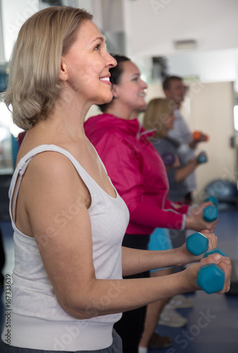elderly female blonde is engaged with dumbbells in modern sports hall
