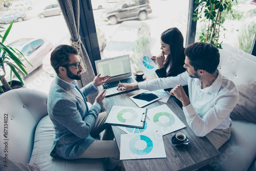 Presentation of a new start up for investors. Three young successful people are discussing numbers in a nice light modern coworking  all in formal wear  concentreted