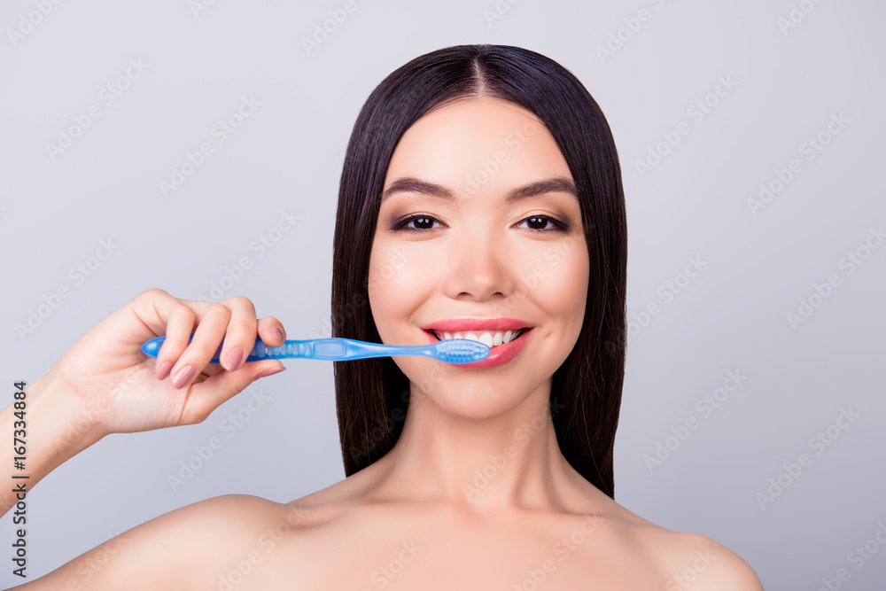 Dental health concept. Gorgeous asian girl is cleaning her teeth with blue tooth brush, on light grey background, she has a beaming smile Dental health concept. Gorgeous asian girl is cleaning her teeth with blue tooth brush, on light grey background, she has a beaming smile