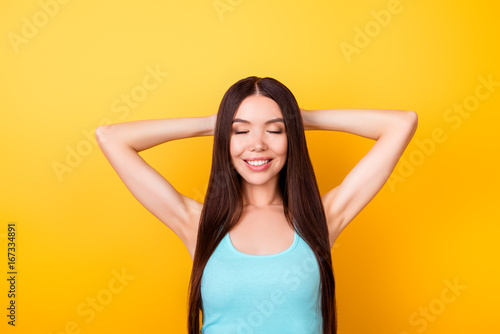 Charming relaxed young asian girl on summer vacation. She is wearing casual blue singlet, has a beaming toothy smile, long nice hair, on bright yellow background