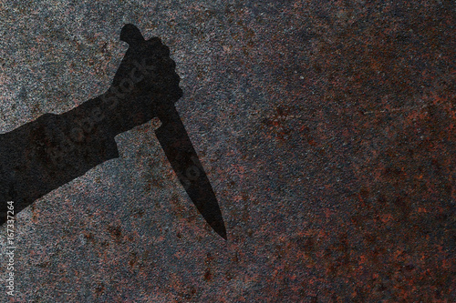 Human hand with killing knife silhouette in shadow on rust wall background. Illustration for criminal news and chronicles.