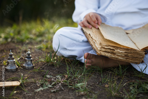 a boy in a kimono sits in a lotus position meditating in autumn, reading old book of wisdom