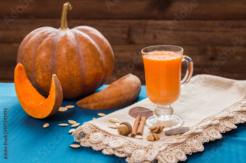 A glass of pumpkin smoothies on a blue background with pieces of pumpkin, nuts and dry leaves