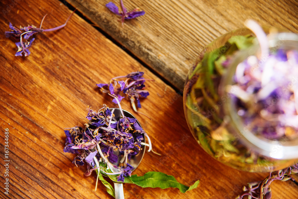 Two glass cups of drink herbal tea. Glass jar on the board with dry herbal tea. Herbal tea is scattered on gray vintage wooden board. Two glass cups of drink herbal tea. Glass jar on the board with dry herbal tea. Herbal tea is scattered on gray vintage wooden board.