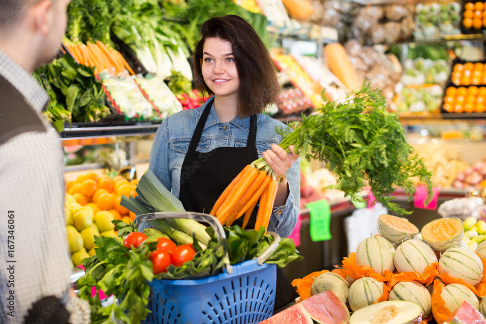 positive female seller assisting customer to buy fruit and vegetables in grocery shop