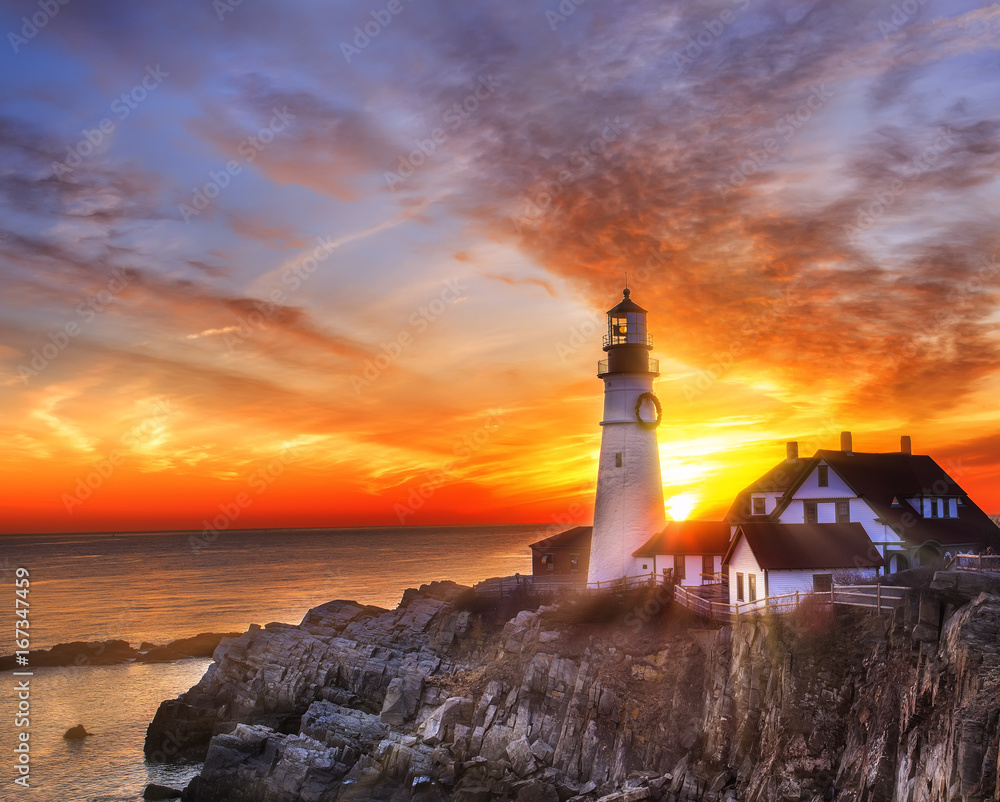  Lighthouse on the beach at dawn. A beautiful coastline covered with stones, the sun's rays illuminating everything around in the early morning. USA. Portland. Maine.
