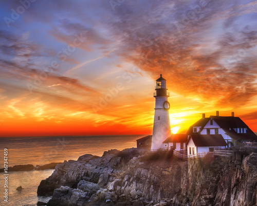  Lighthouse on the beach at dawn. A beautiful coastline covered with stones, the sun's rays illuminating everything around in the early morning. USA. Portland. Maine. 