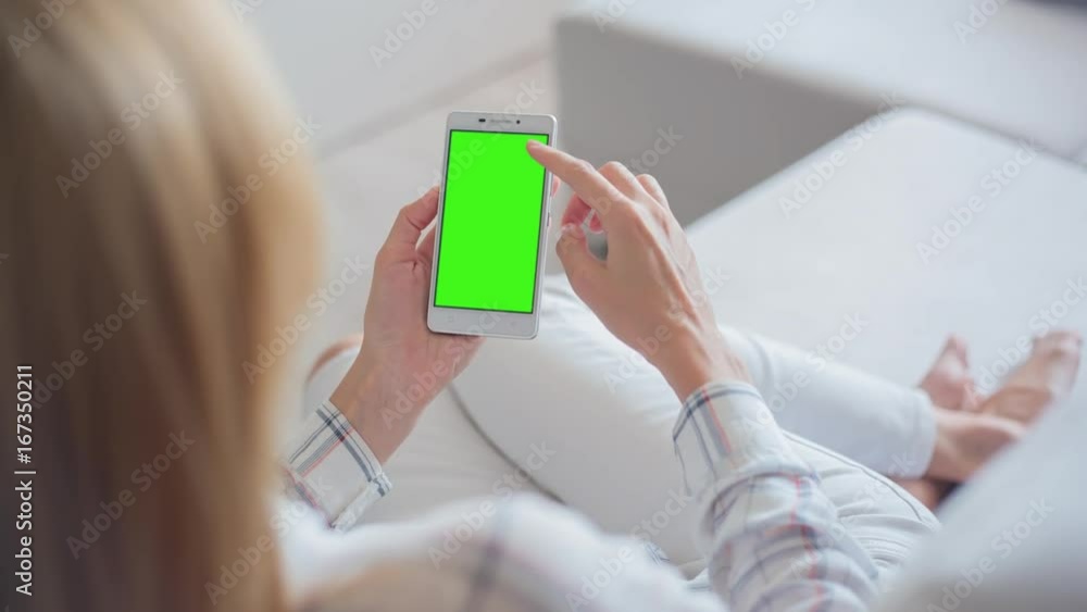 Young Woman in white jeans laying on couch uses smartphone with pre-keyed green screen. Few types of gestures - scrolling up and down, tapping, zoom in and out. Perfect for screen compositing Young Woman in white jeans laying on couch uses smartphone with pre-keyed green screen. Few types of gestures - scrolling up and down, tapping, zoom in and out. Perfect for screen compositing