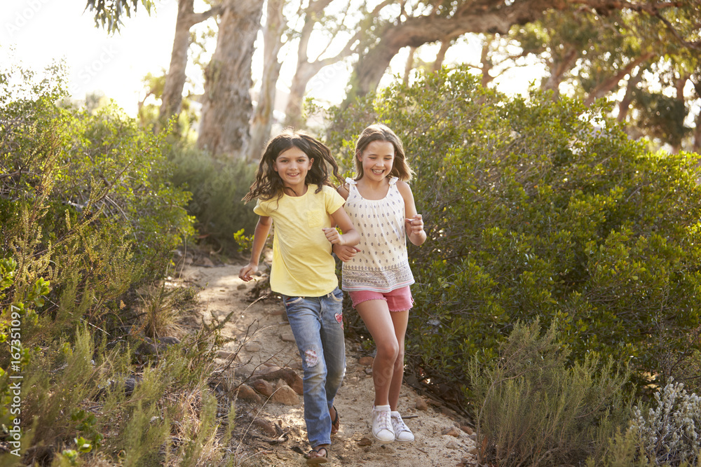 Two smiling young girls running in a forest in the sun