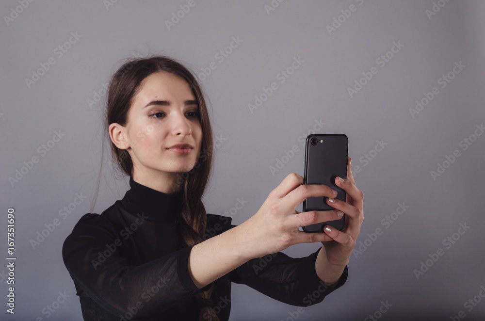 Portrait of a young attractive girl making selfie photo with smartphone isolated on a neutral gray background. Portrait of a young attractive girl making selfie photo with smartphone isolated on a neutral gray background.