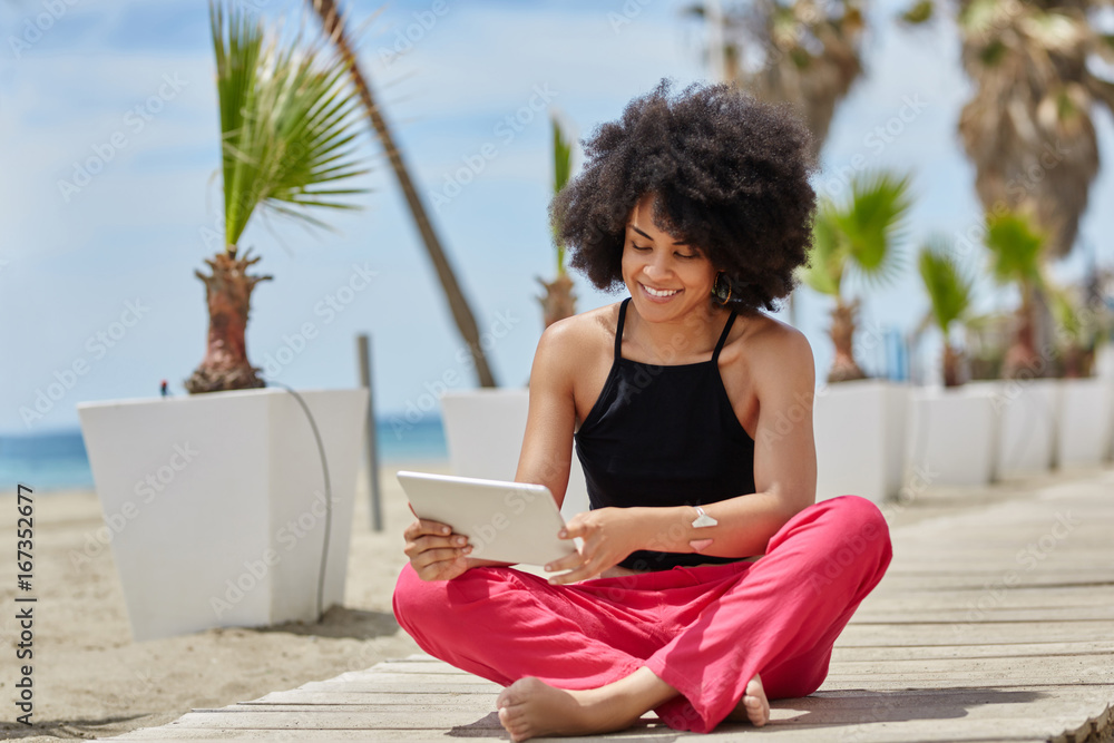 Happy afro american woman sitting crossed legs using tablet