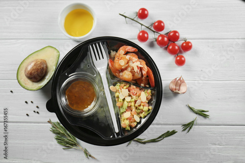 Plastic container with delicious food on wooden table