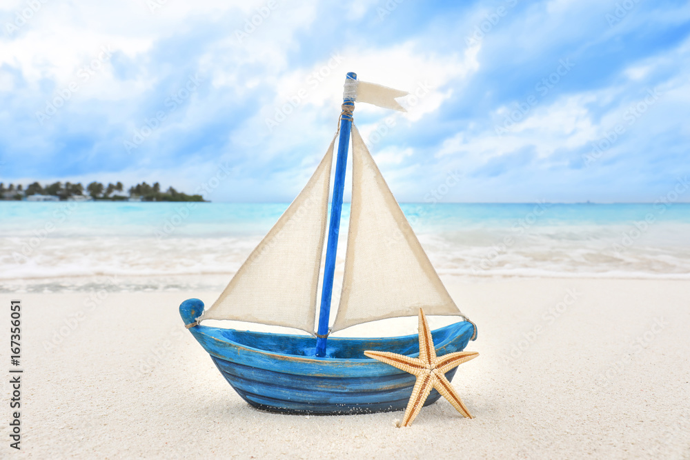 Obraz premium Small toy ship and starfish on sea beach. Summer vacation concept