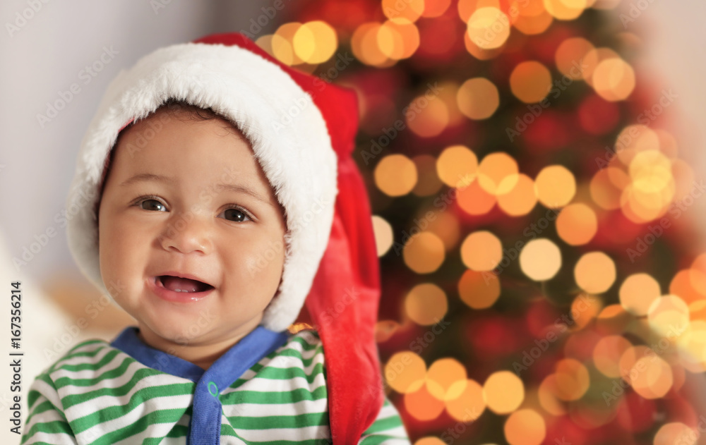 Cute little baby in Santa hat against blurred Christmas lights Cute little baby in Santa hat against blurred Christmas lights