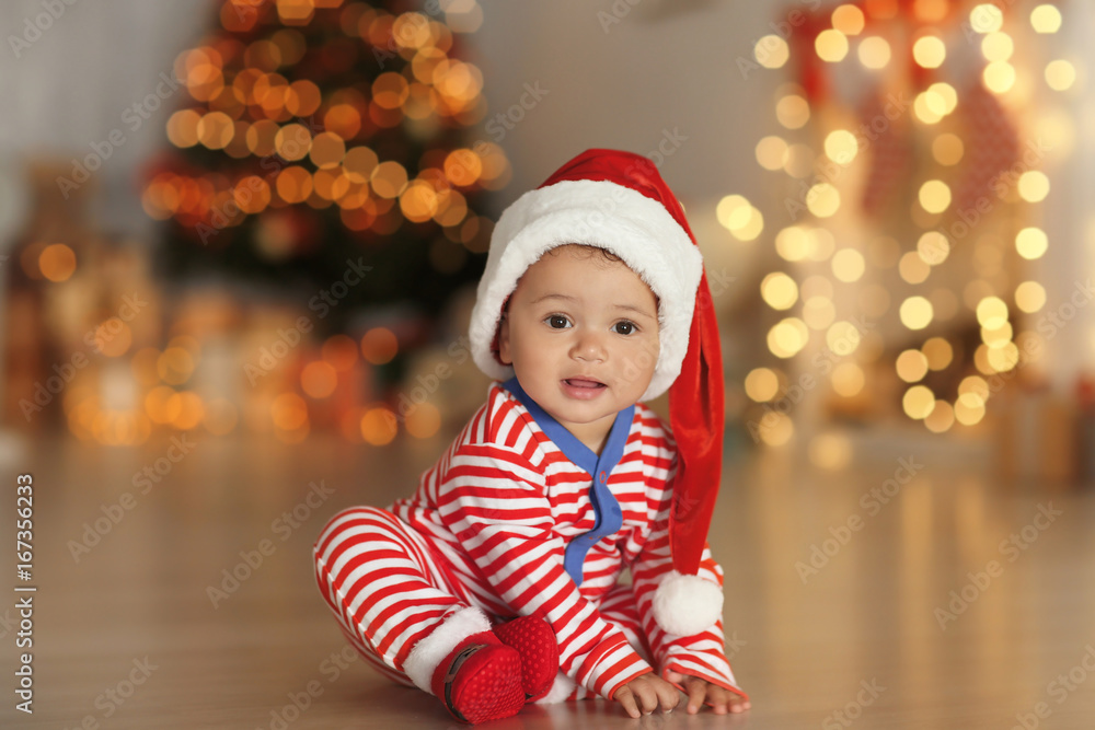 Cute little baby with Santa hat on floor and blurred Christmas lights on background Cute little baby with Santa hat on floor and blurred Christmas lights on background