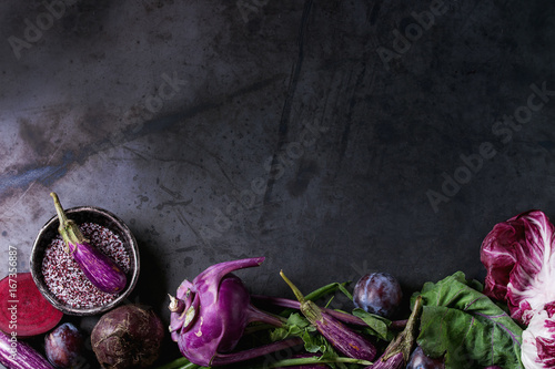 Assortment raw organic of purple vegetables mini eggplants, spring onion, beetroot, radicchio salad, plums, kohlrabi, flower salt over dark metal background. Top view with space. Food frame