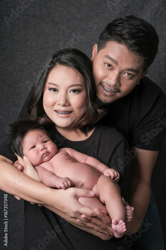 family portrait of young asian mum and dad and boy newborn in black background .