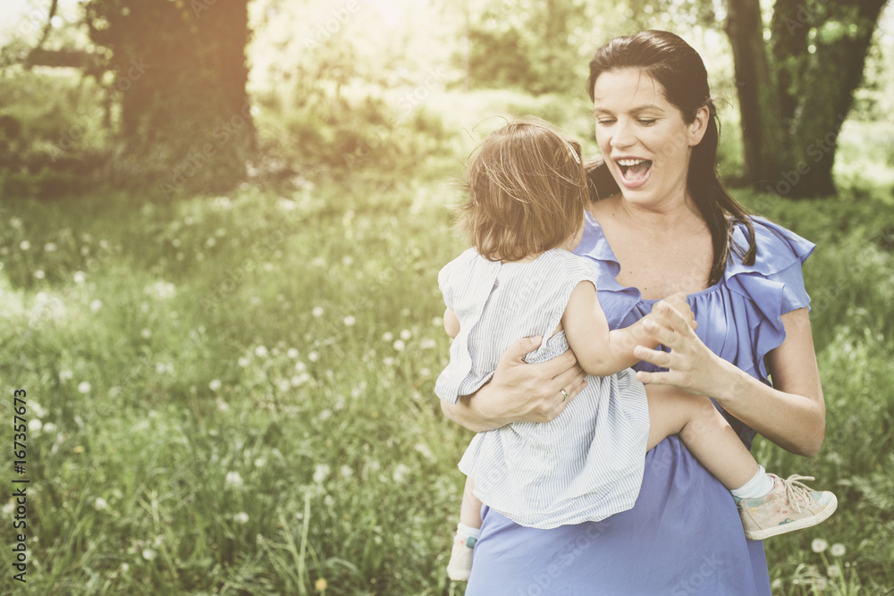 Fototapeta premium Pregnant mother playing with little daughter in park. Mother and daughter in meadow.