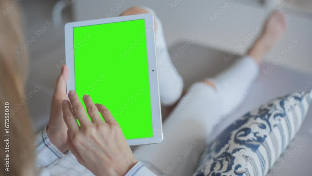 Young Woman in white jeans laying on couch uses Tablet PC with pre-keyed green screen. Few types of gestures - scrolling up and down, tapping, zoom in and out. Perfect for screen compositing Young Woman in white jeans laying on couch uses Tablet PC with pre-keyed green screen. Few types of gestures - scrolling up and down, tapping, zoom in and out. Perfect for screen compositing
