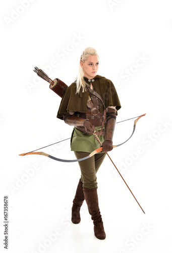 full length portrait of a blonde girl wearing green and brown medieval costume, holding a bow and arrow. isolated on white background.