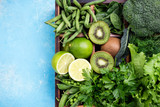 Green vegetables background. Fresh garden produce. Broccoli, spinach, kiwi, lettuce, parsley, dill, asparagus beans on blue concrete background, top view and copy space